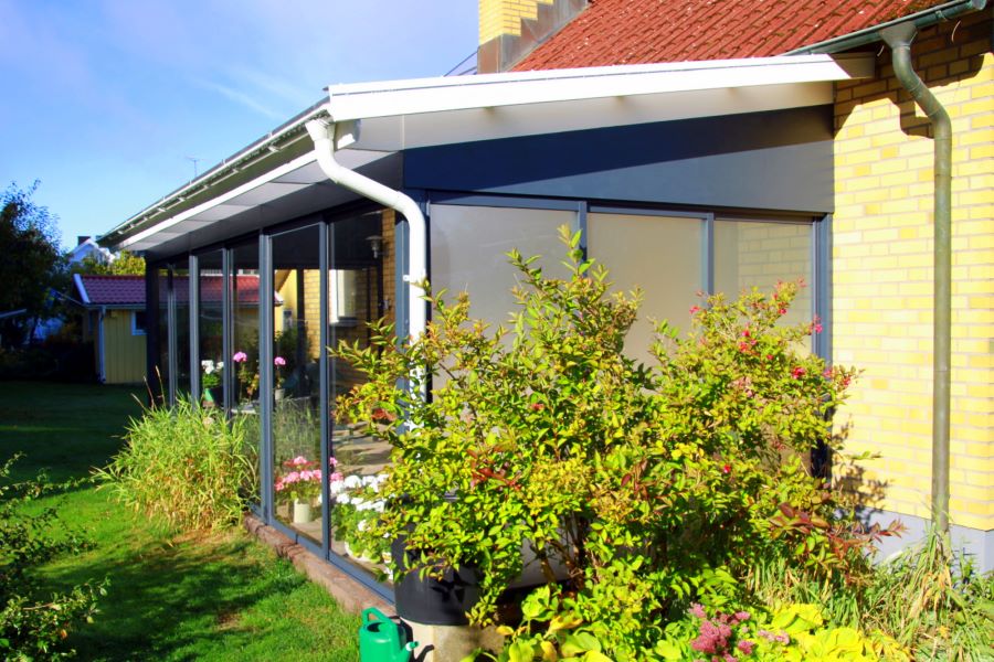 Uterum med skjutdörrar i frostat glas för insynsskydd, anslutet till ett gult tegelhus och omgiven av en välskött trädgård med buskar och blommor | Sommar M50 glaspartier | Mekoflex Uterum