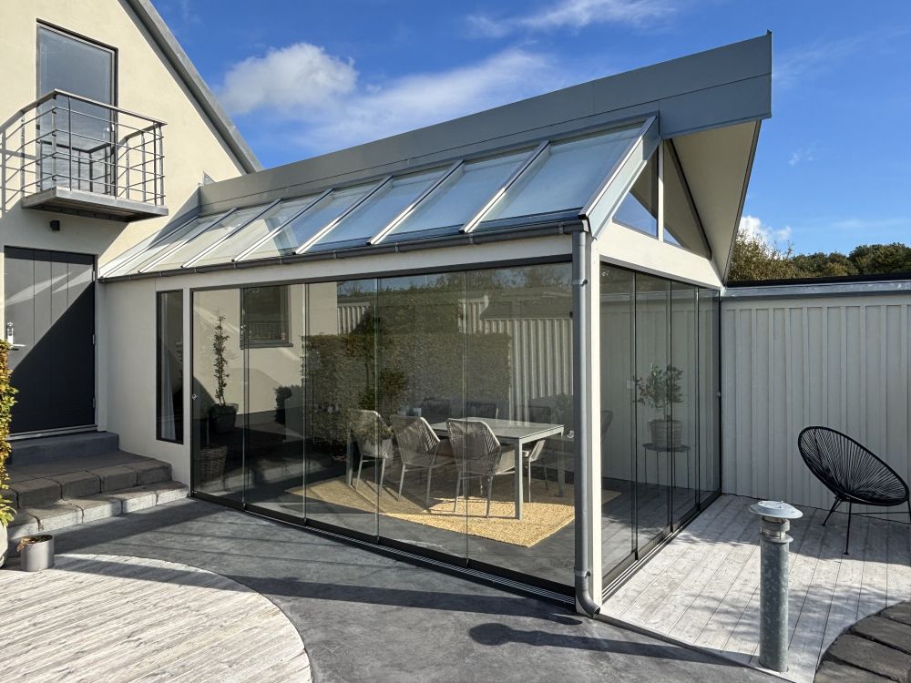 Stilrent uterum med ett 5-delat, ramlöst skjutdörrsparti som kan skjutas åt sidan för att öppna upp hela väggen. Glaspartiet ger ett generöst ljusinsläpp och kopplar samman uteplats och inomhusmiljö.