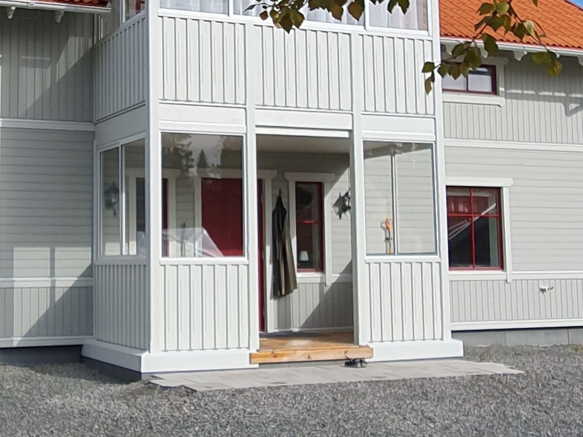 Inglasad farstukvist med glaspartier på ett ljust trähus med röda detaljer. En välkomnande entré med skydd mot väder och vind.