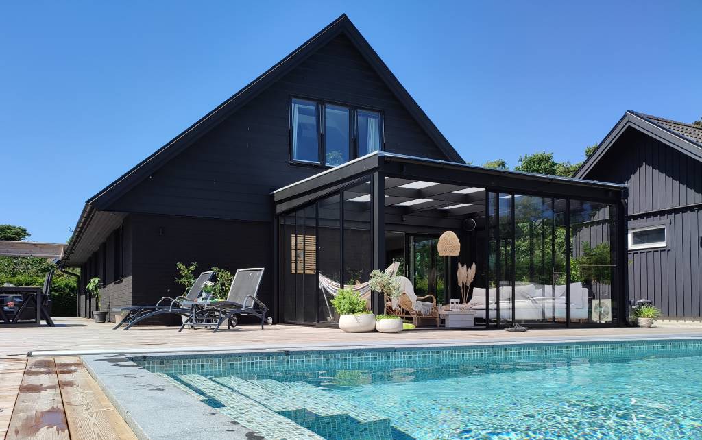Fint sommaruterum med turkosskimrande pool och trädäck som binder samman poolen och huset. Måttanpassade skjutdörrar i svart färg och isolerat kanaltak. | Mekoflex Uterum