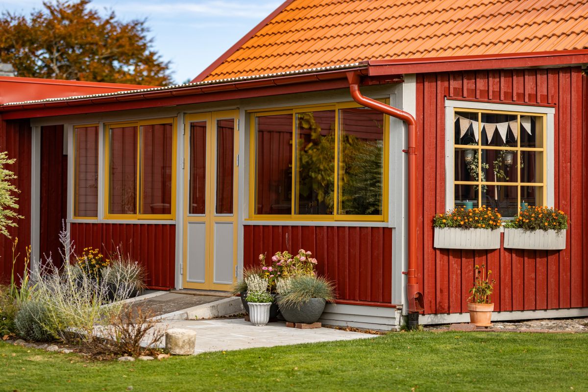 Skjutfönster lackerade i ockragul färg till charmigt uterum med klassiskt röd träfasad.