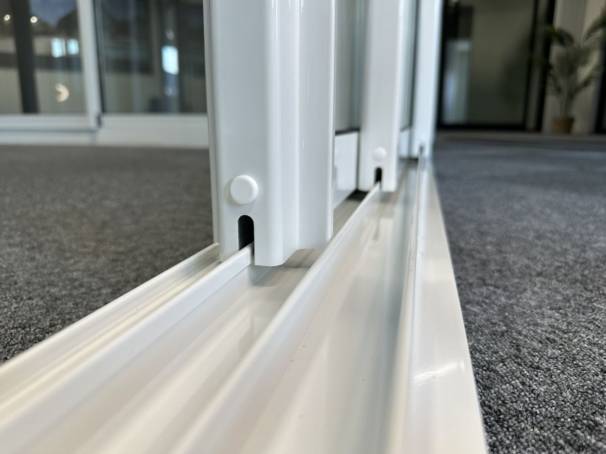 Närbild på undre räls där vita skjutdörrar löper på kullagrade hjul längs spåren, vilket ger en smidig och lättmanövrerad öppning. Bilden visar detaljkvalitet och precision i Mekoflex skjutpartier för uterum och altan.