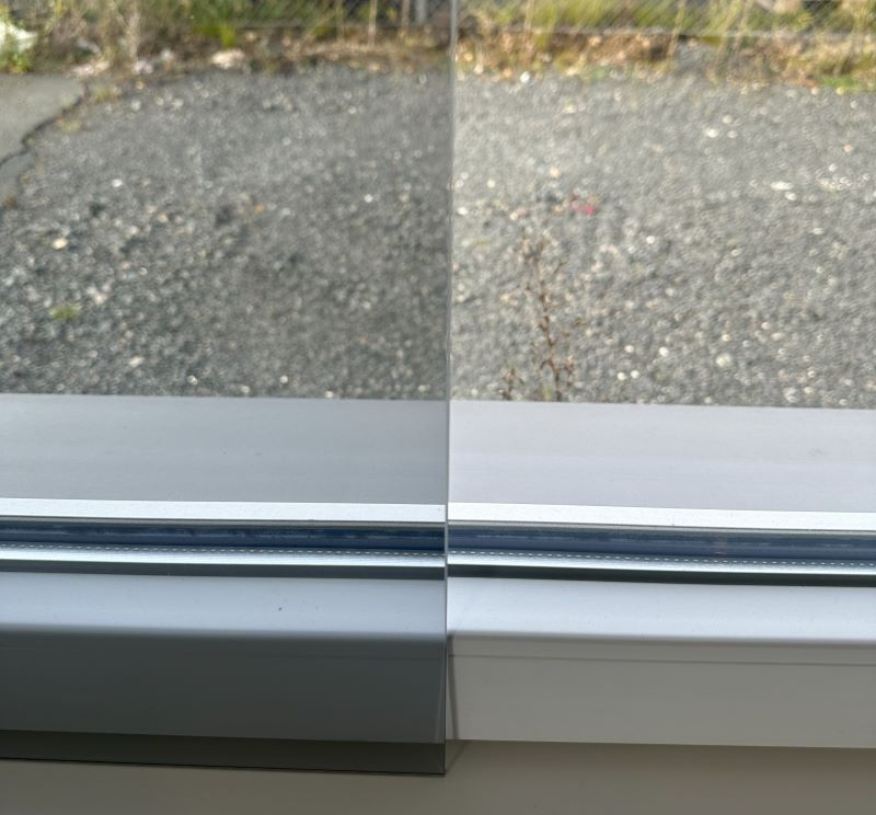 Närbild på en tonad glasruta placerad framför ett vanligt fönsterglas, demonstrerar skillnaden i transparens och färg för att jämföra effekten av toning mot standardglas, med grusig mark i bakgrunden. | Mekoflex Uterum