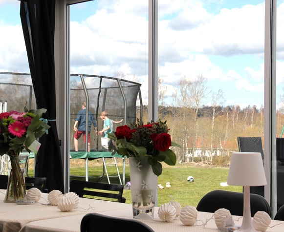 Vår/Höst M70 glaspartier - Vår/Höst M70 skjutdörrar sett inifrån uterummet med utsikt över trädgården och barn som leker. | Mekoflex Uterum
